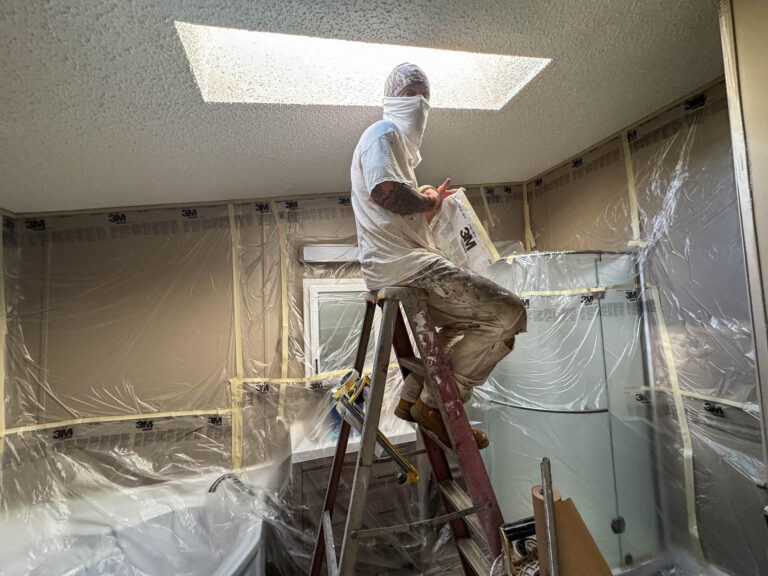 A painter on a ladder masking a bathroom before spray painting